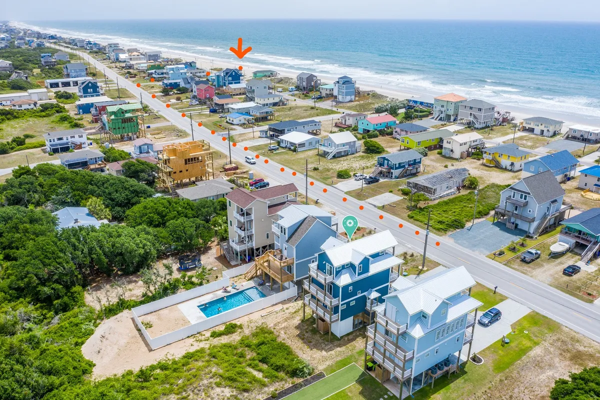 A vibrant exterior shot featuring beachfront houses, a clear ocean view, a swimming pool, and a road leading directly to the beach. The setting is ideal for beach activities, walks, and family gatherings, encapsulating the accessibility to outdoor, dog-friendly adventures.