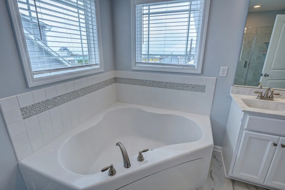 A spacious bathroom showcasing a luxurious whirlpool tub, decorative tiled walls, and large windows that flood the space with natural light. The setting is both elegant and inviting, designed for ultimate relaxation and rejuvenation.