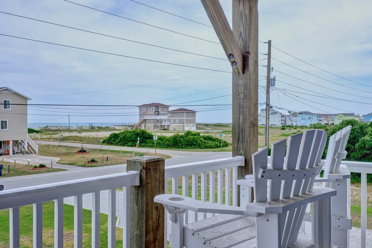 A wooden deck with comfortable deck chairs overlooks the ocean, with greenery and neighboring homes in the distance. The space is designed for relaxation, offering a tranquil setting for enjoying the coastal views, sunset, or morning coffee.