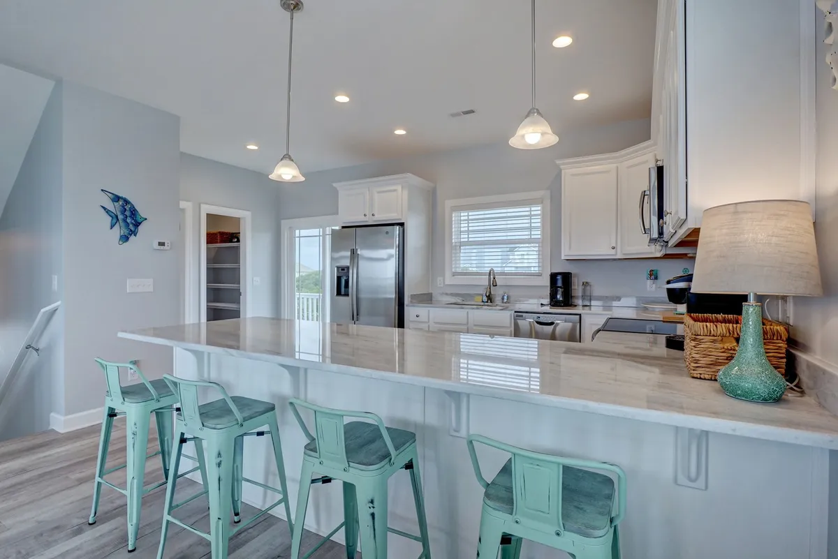 A bright, modern kitchen with a spacious island and cheerful bar stools, complete with appliances and playful decorative touches. The room is set up for gathering, cooking, and sharing meals.