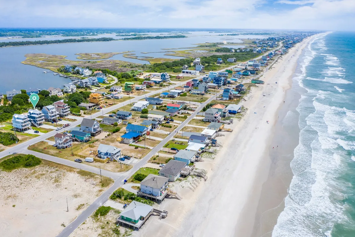 A scenic perspective showing beachfront properties, a wide sandy beach, sparkling ocean, and adjacent marshland, representing the local environment and nearby accessible attractions.