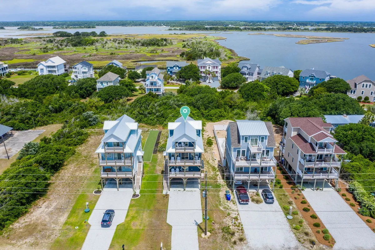 Three charming beach houses sit amid lush greenery, with calm waters of the intracoastal waterway in the background. The serene atmosphere invites guests to imagine sunset strolls and waterfront activities right outside their door.