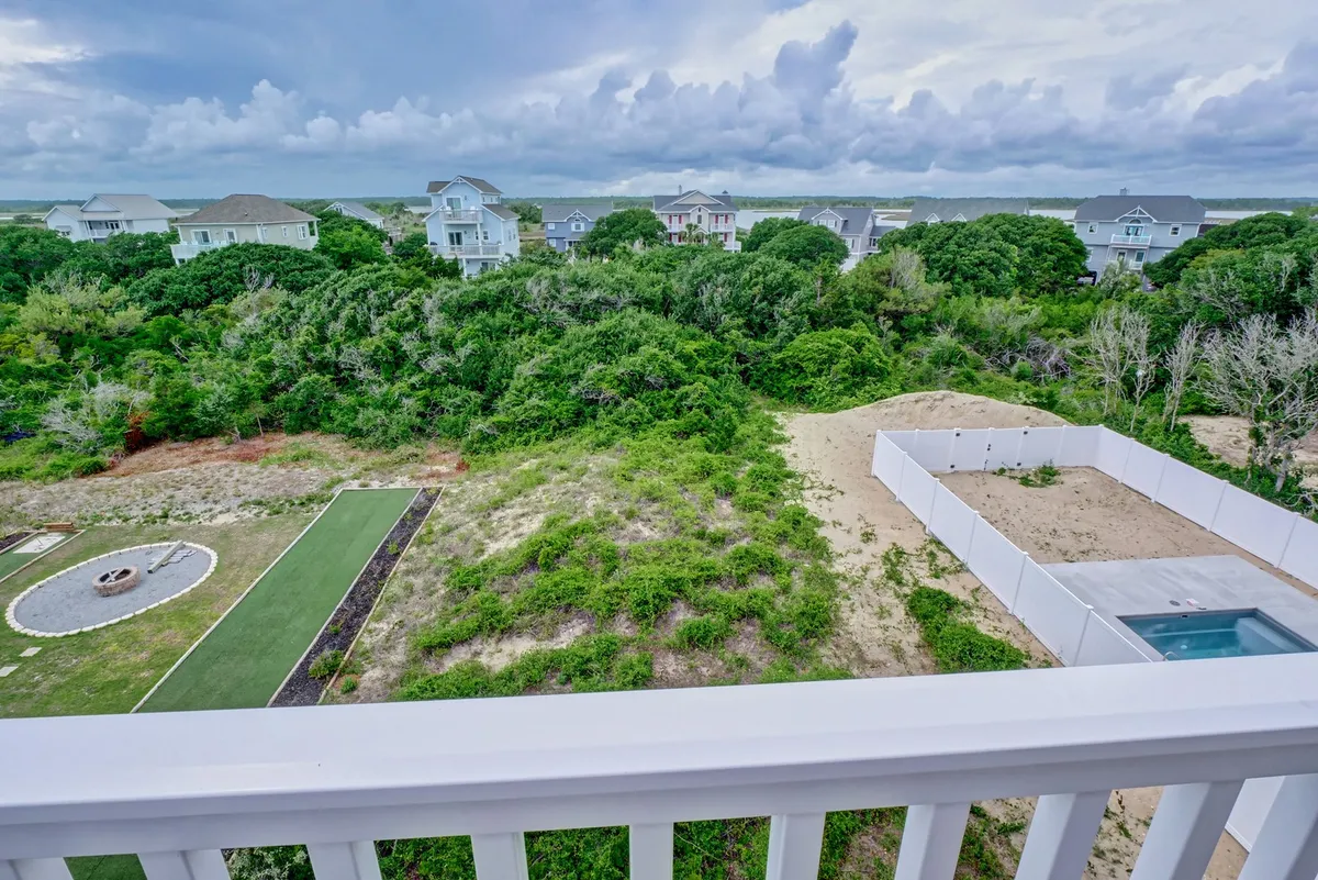 A landscaped backyard features a cozy fire pit area and a pool, surrounded by lush plantings and residential buildings. The space feels private and inviting, ideal for stargazing, sharing drinks, or simply unwinding outdoors.