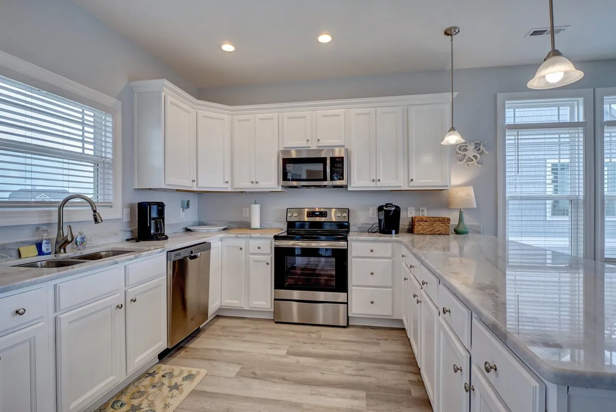 A bright, airy kitchen with white cabinetry, stainless steel appliances, marble countertops, and a large window, creating a welcoming environment for cooking, socializing, and daily living. The space feels practical yet polished, enhancing the sense of everyday ease.