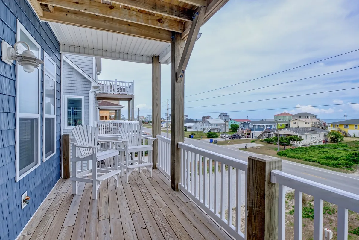 A cozy porch setup with white outdoor chairs and a wooden railing, overlooking neighboring houses. The inviting space is ideal for relaxing with a morning coffee or lounging with a pet after playtime outdoors.